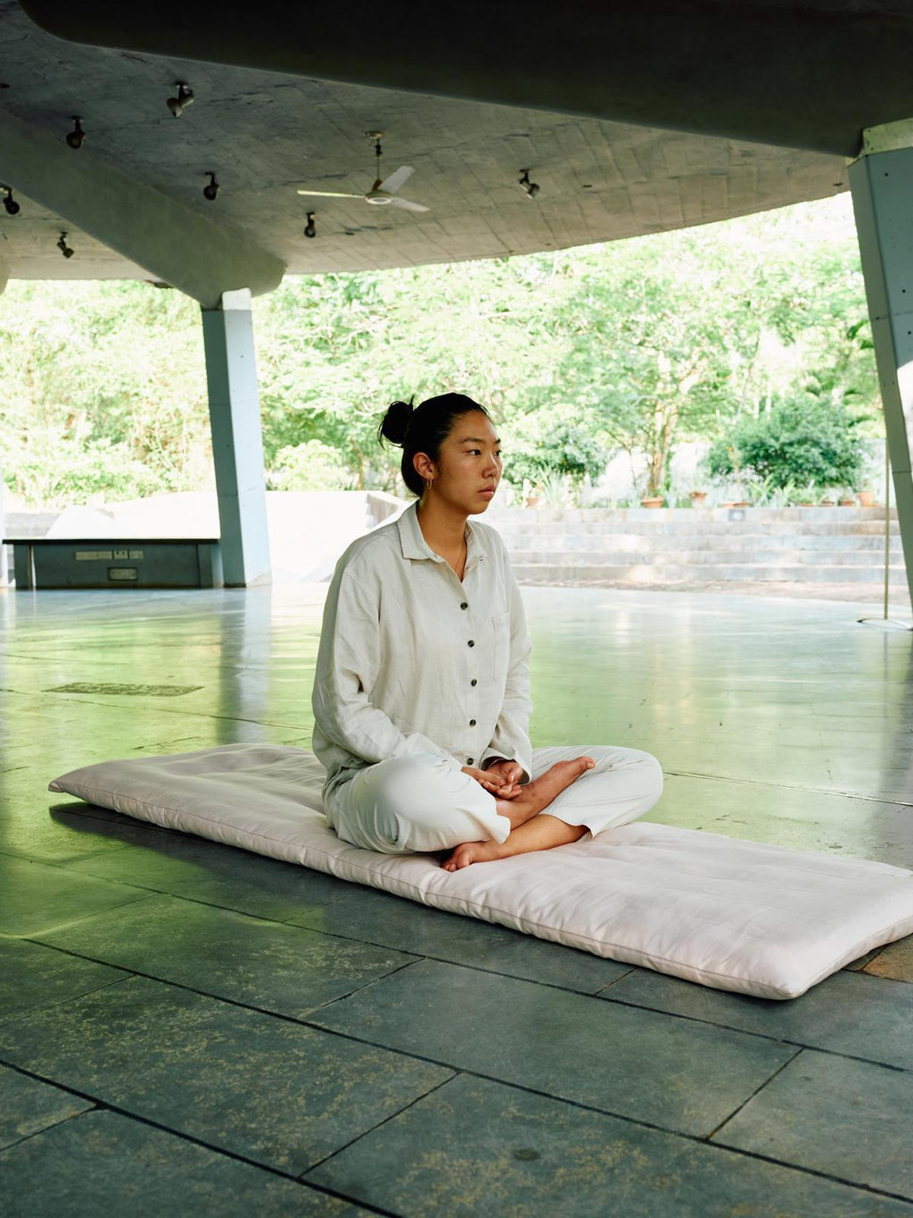 Person meditating on a mat in a modern architectural setting with greenery.