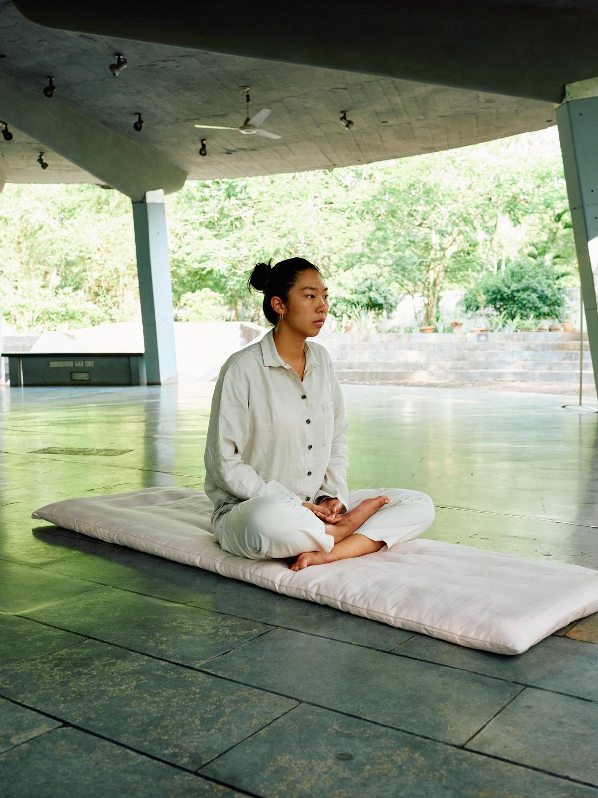 Person meditating on a mat in a modern architectural setting with greenery.